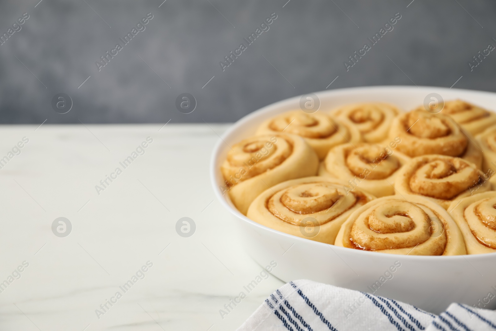 Photo of Raw cinnamon rolls in baking dish on white marble table, closeup. Space for text