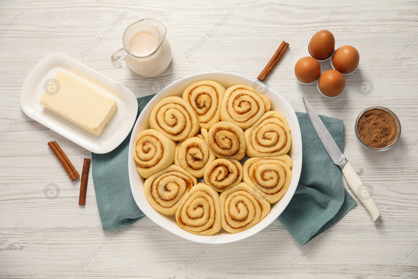 Photo of Raw cinnamon rolls and different ingredients on light wooden table, flat lay