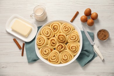 Raw cinnamon rolls and different ingredients on light wooden table, flat lay