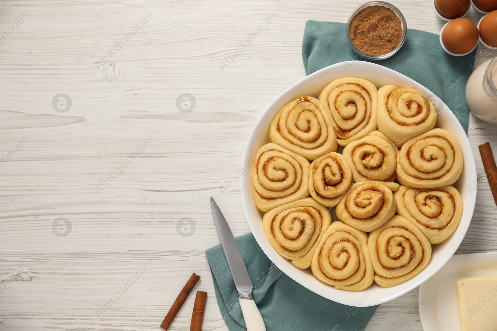 Photo of Raw cinnamon rolls and different ingredients on light wooden table, flat lay. Space for text