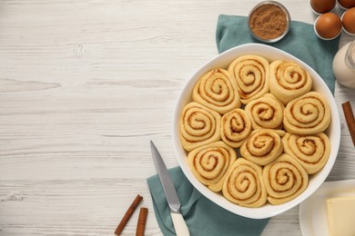 Raw cinnamon rolls and different ingredients on light wooden table, flat lay. Space for text