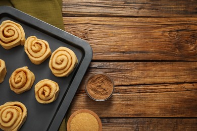 Photo of Raw cinnamon rolls, cocoa powder and brown sugar on wooden table, flat lay. Space for text