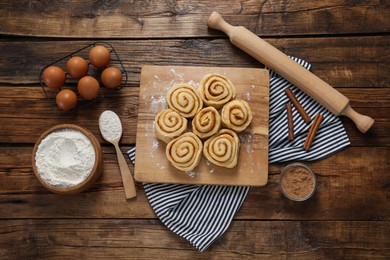 Photo of Raw cinnamon rolls and different ingredients on wooden table, flat lay