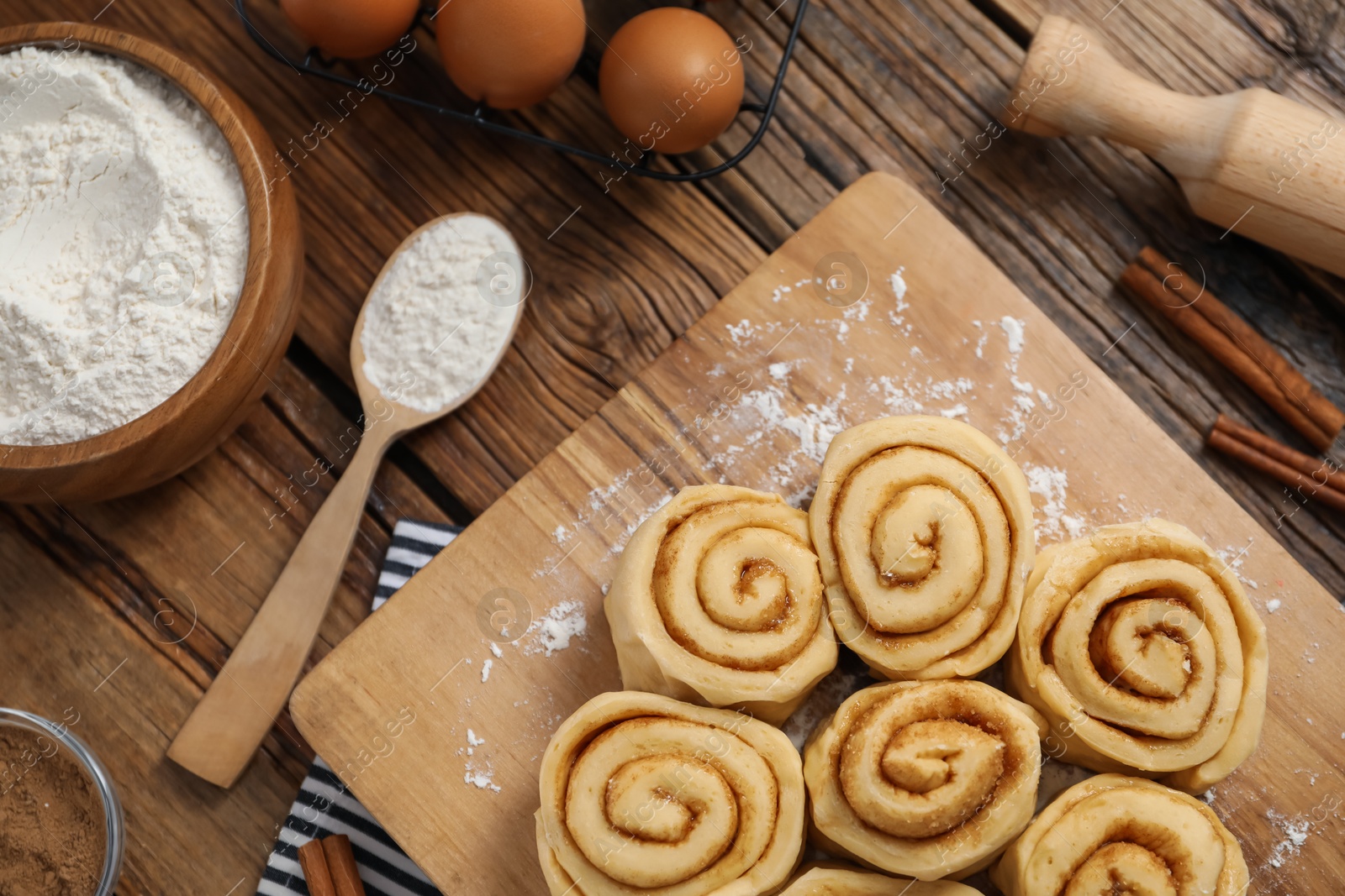 Photo of Raw cinnamon rolls and different ingredients on wooden table, flat lay