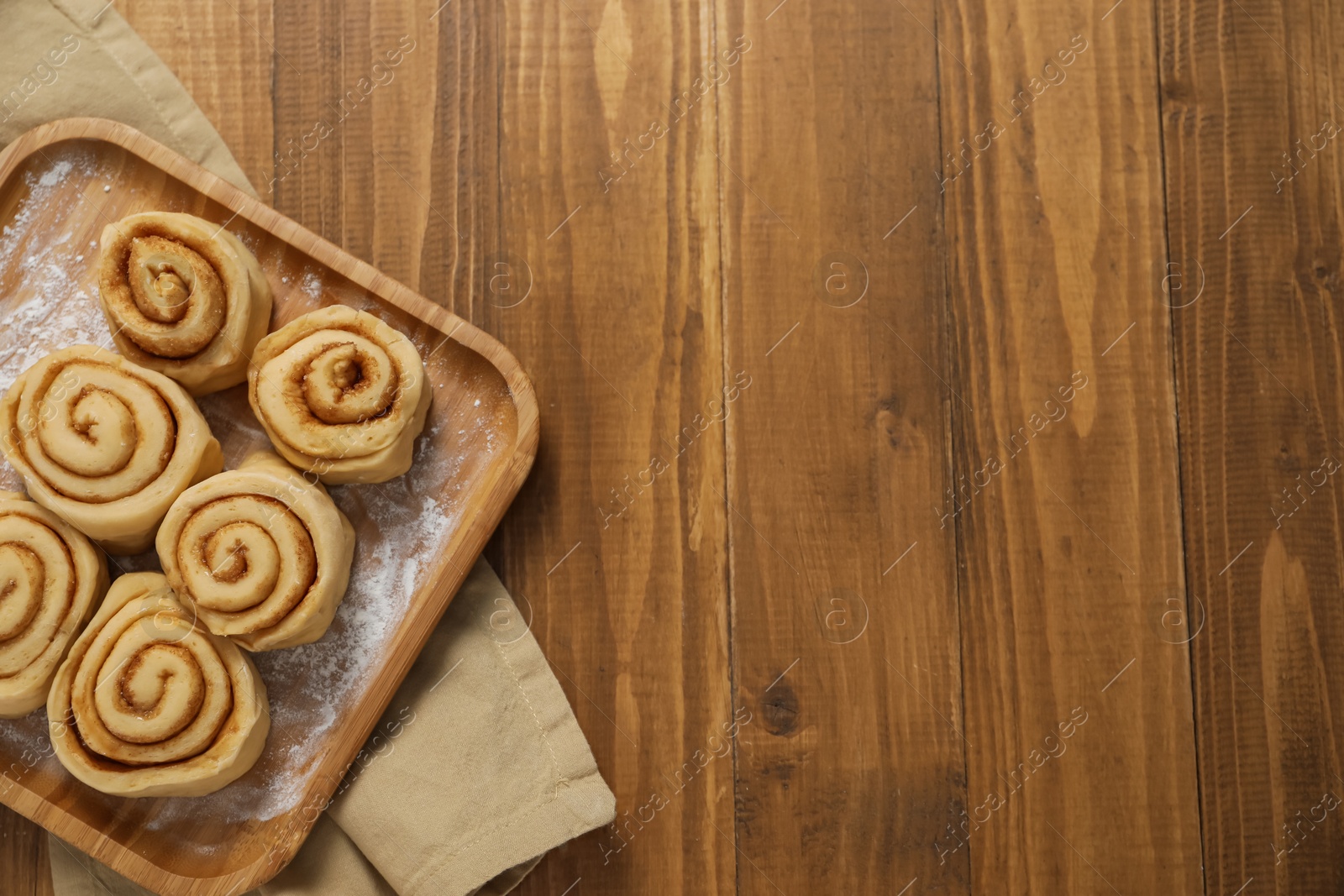 Photo of Raw cinnamon rolls on wooden table, top view. Space for text