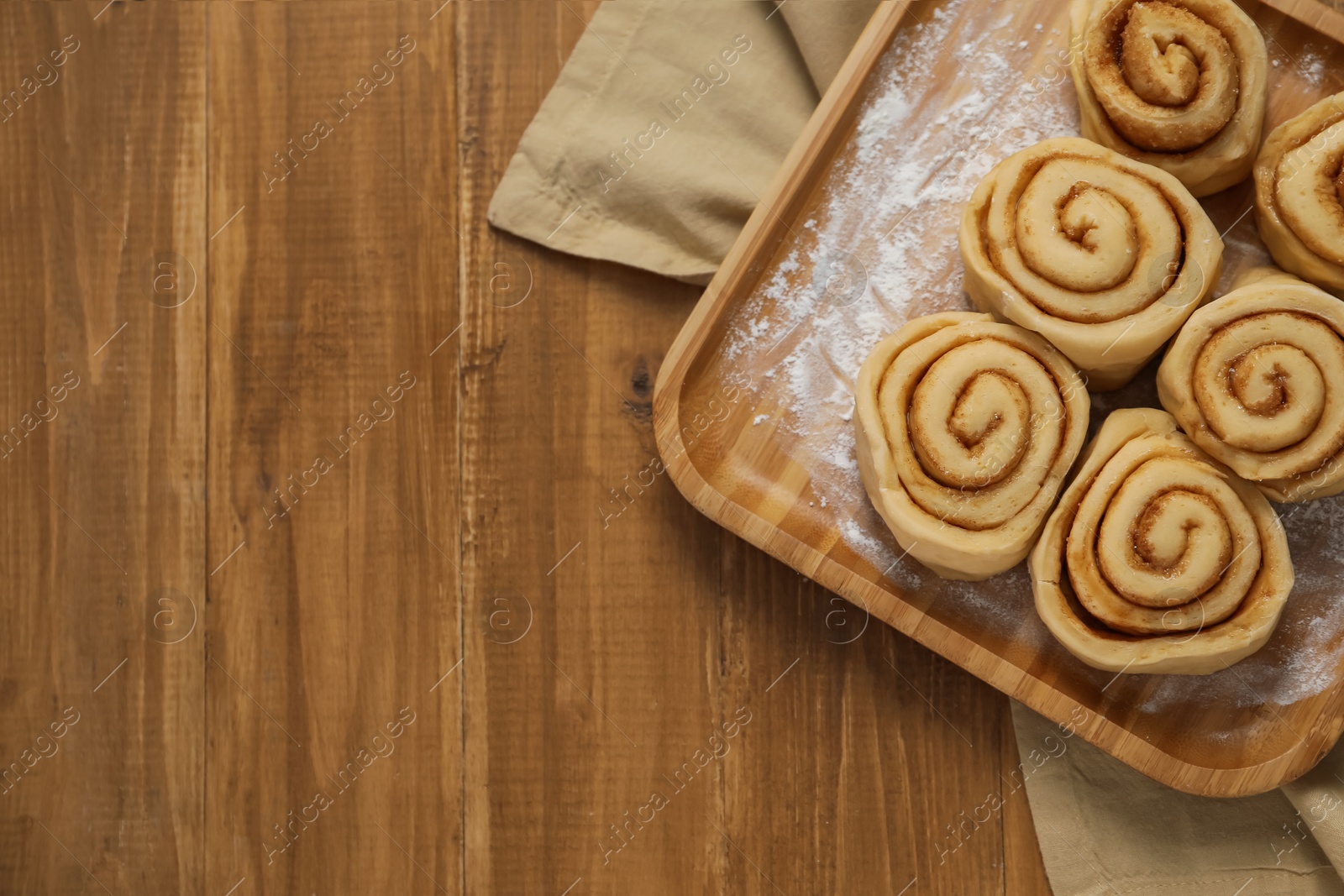 Photo of Raw cinnamon rolls on wooden table, top view. Space for text