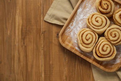 Raw cinnamon rolls on wooden table, top view. Space for text