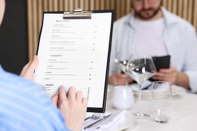 Couple choosing dishes from menu at table in restaurant, closeup