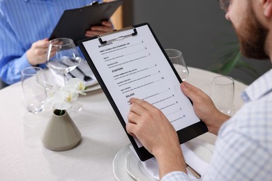 Photo of Couple choosing dishes from menu at table in restaurant, closeup