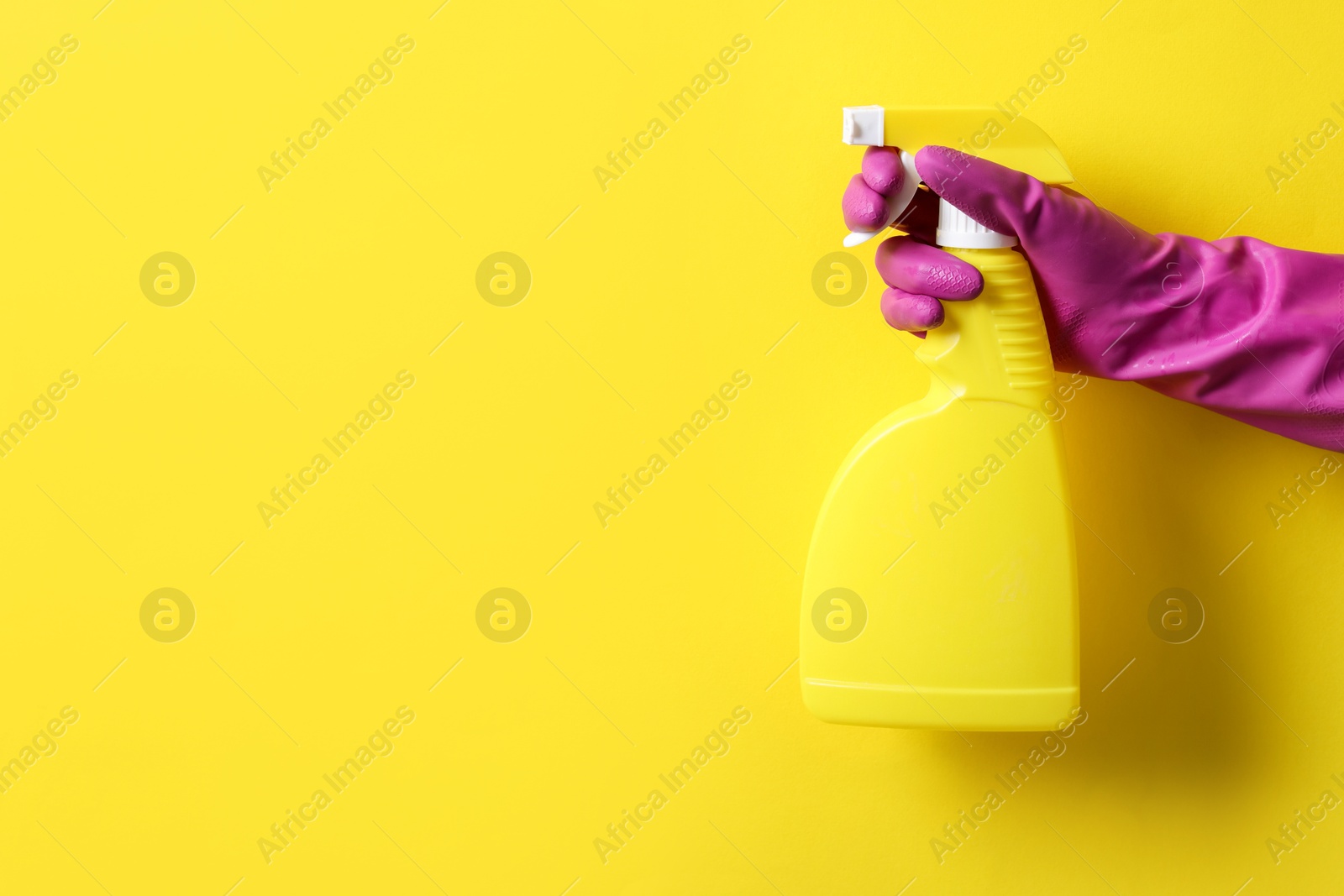 Photo of Woman with spray bottle of cleaning product on yellow background, closeup. Space for text