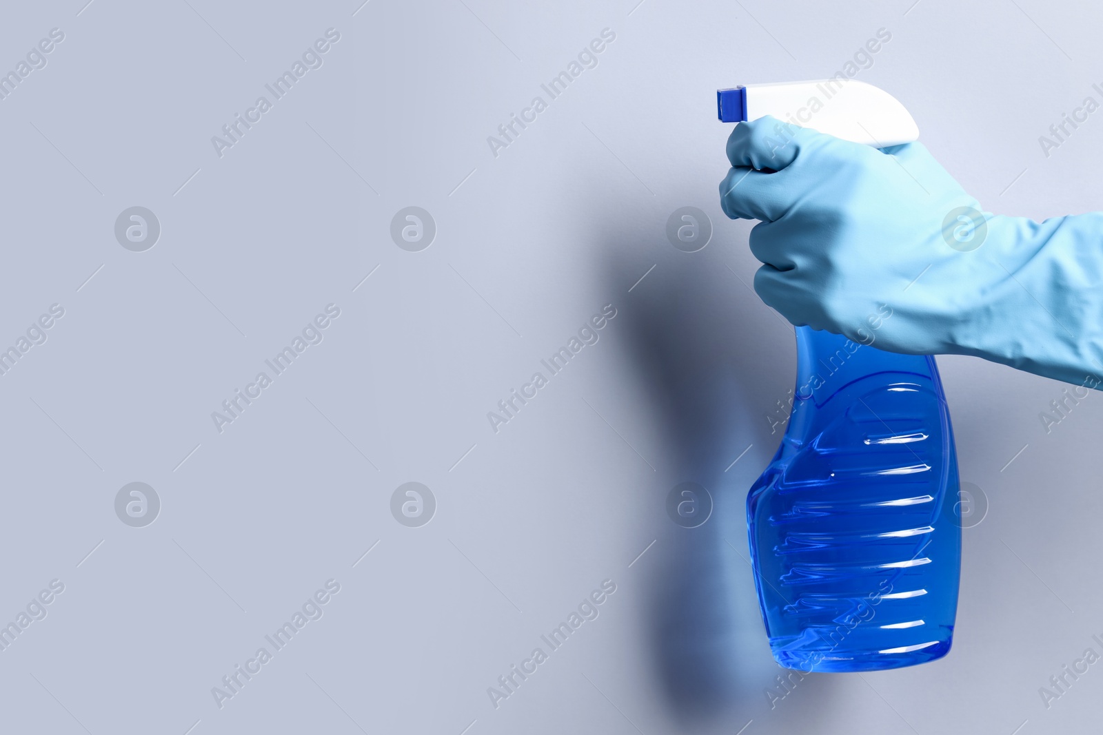 Photo of Woman with spray bottle of cleaning product on light grey background, closeup. Space for text