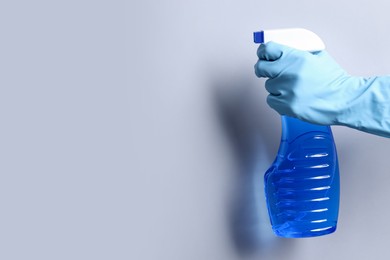 Photo of Woman with spray bottle of cleaning product on light grey background, closeup. Space for text