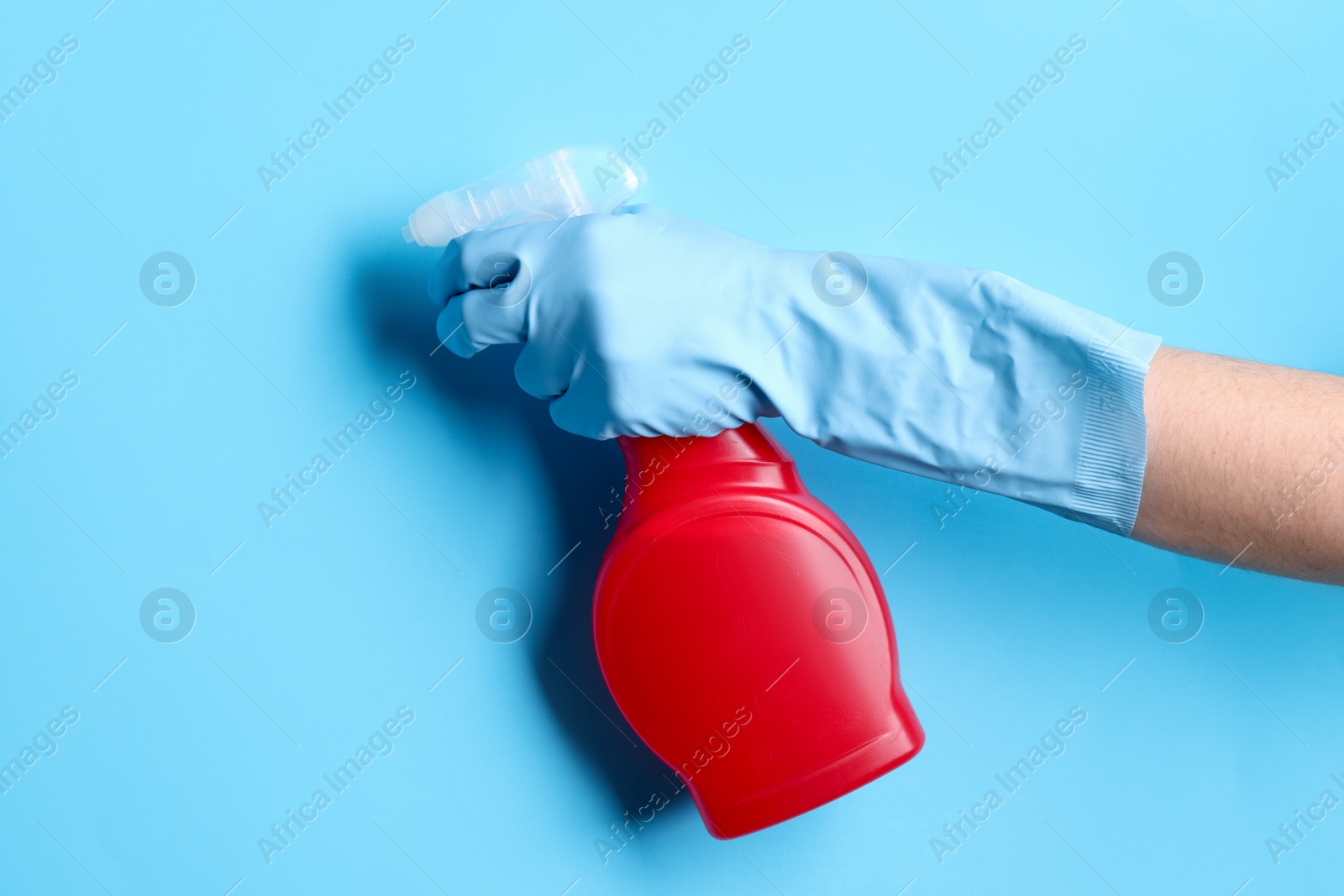 Photo of Woman with spray bottle of cleaning product on light blue background, closeup