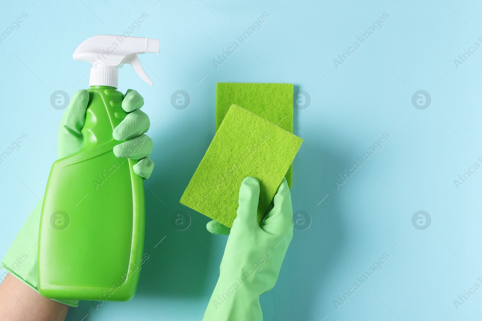 Photo of Woman with bottle of cleaning product and sponges on light blue background, top view. Space for text