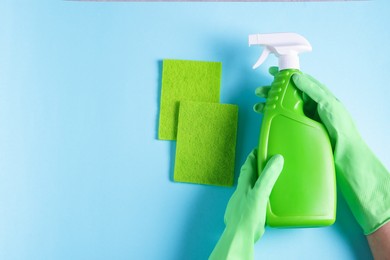 Photo of Woman with bottle of cleaning product and sponges on light blue background, top view. Space for text