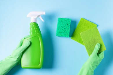 Photo of Woman with bottle of cleaning product and sponges on light blue background, top view