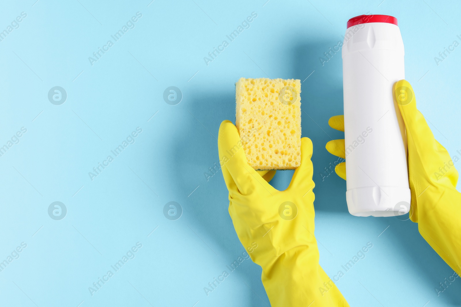 Photo of Woman with bottle of cleaning product and sponge on light blue background, top view. Space for text