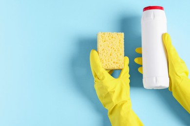 Photo of Woman with bottle of cleaning product and sponge on light blue background, top view. Space for text