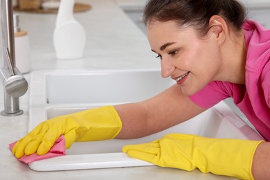 Woman cleaning sink with rag in kitchen