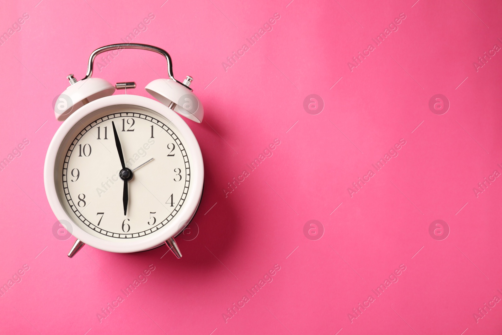 Photo of White alarm clock on pink background, top view. Space for text