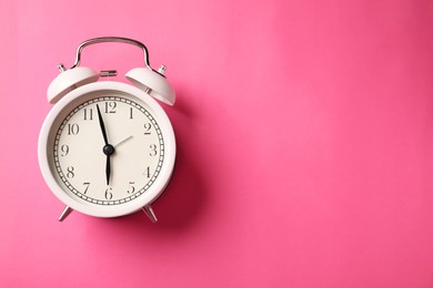 Photo of White alarm clock on pink background, top view. Space for text