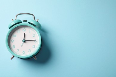 Photo of Turquoise alarm clock on light blue background, top view. Space for text