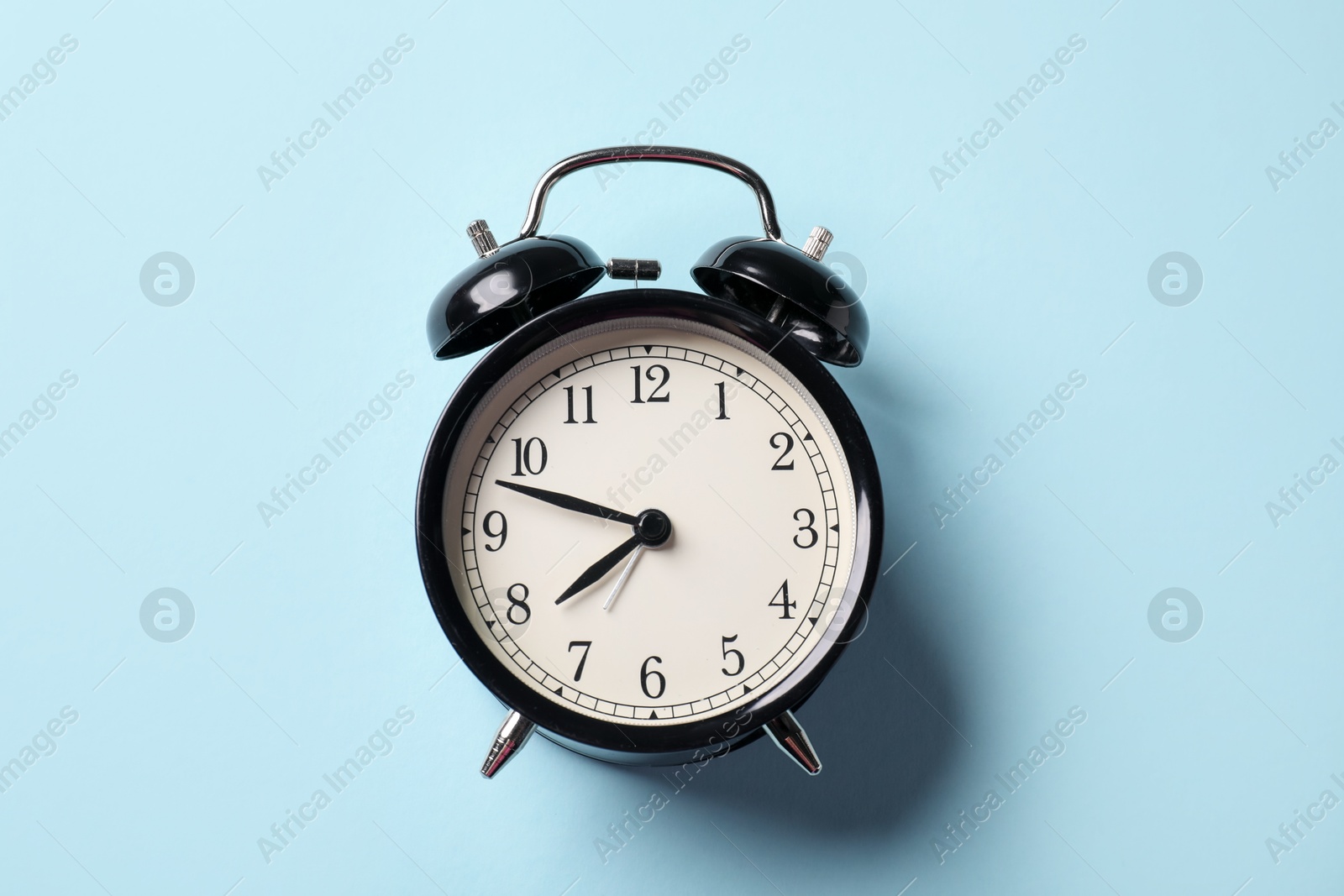 Photo of Black alarm clock on light blue background, top view