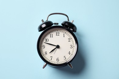 Photo of Black alarm clock on light blue background, top view