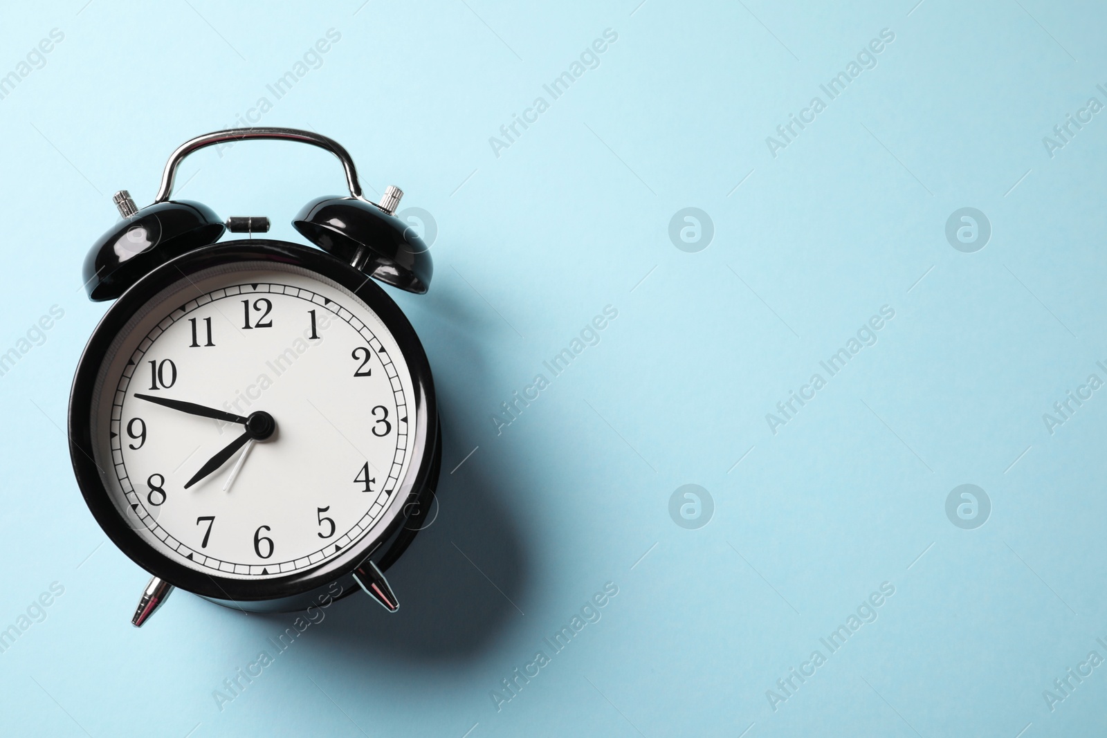 Photo of Black alarm clock on light blue background, top view. Space for text