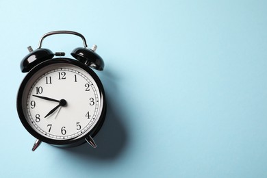 Photo of Black alarm clock on light blue background, top view. Space for text