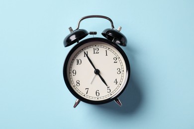 Photo of Black alarm clock on light blue background, top view