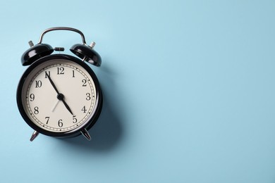 Photo of Black alarm clock on light blue background, top view. Space for text