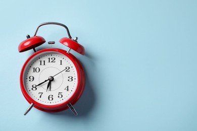 Photo of Red alarm clock on light blue background, top view. Space for text