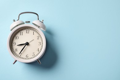 Photo of White alarm clock on light blue background, top view. Space for text