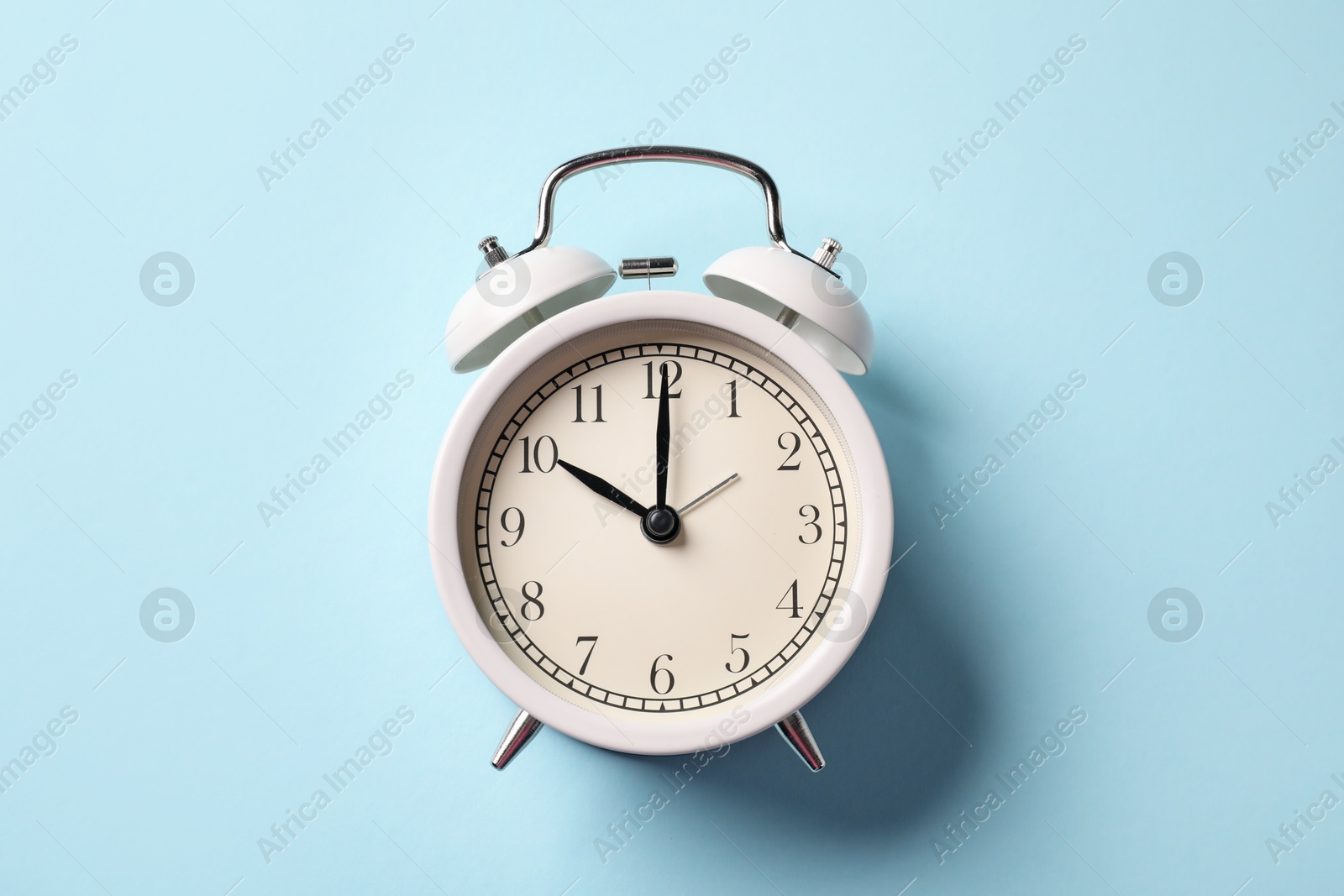 Photo of White alarm clock on light blue background, top view