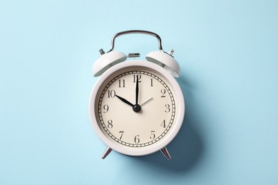 Photo of White alarm clock on light blue background, top view