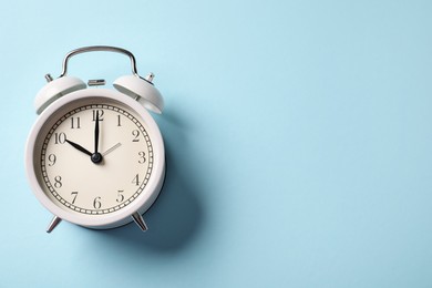 Photo of White alarm clock on light blue background, top view. Space for text