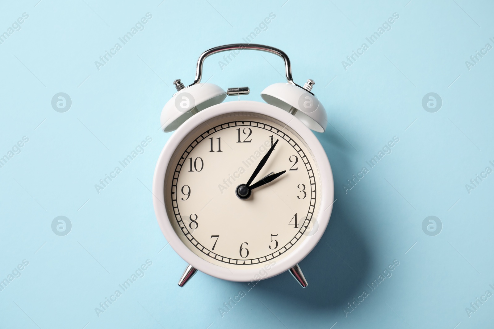 Photo of White alarm clock on light blue background, top view