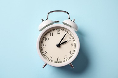 Photo of White alarm clock on light blue background, top view