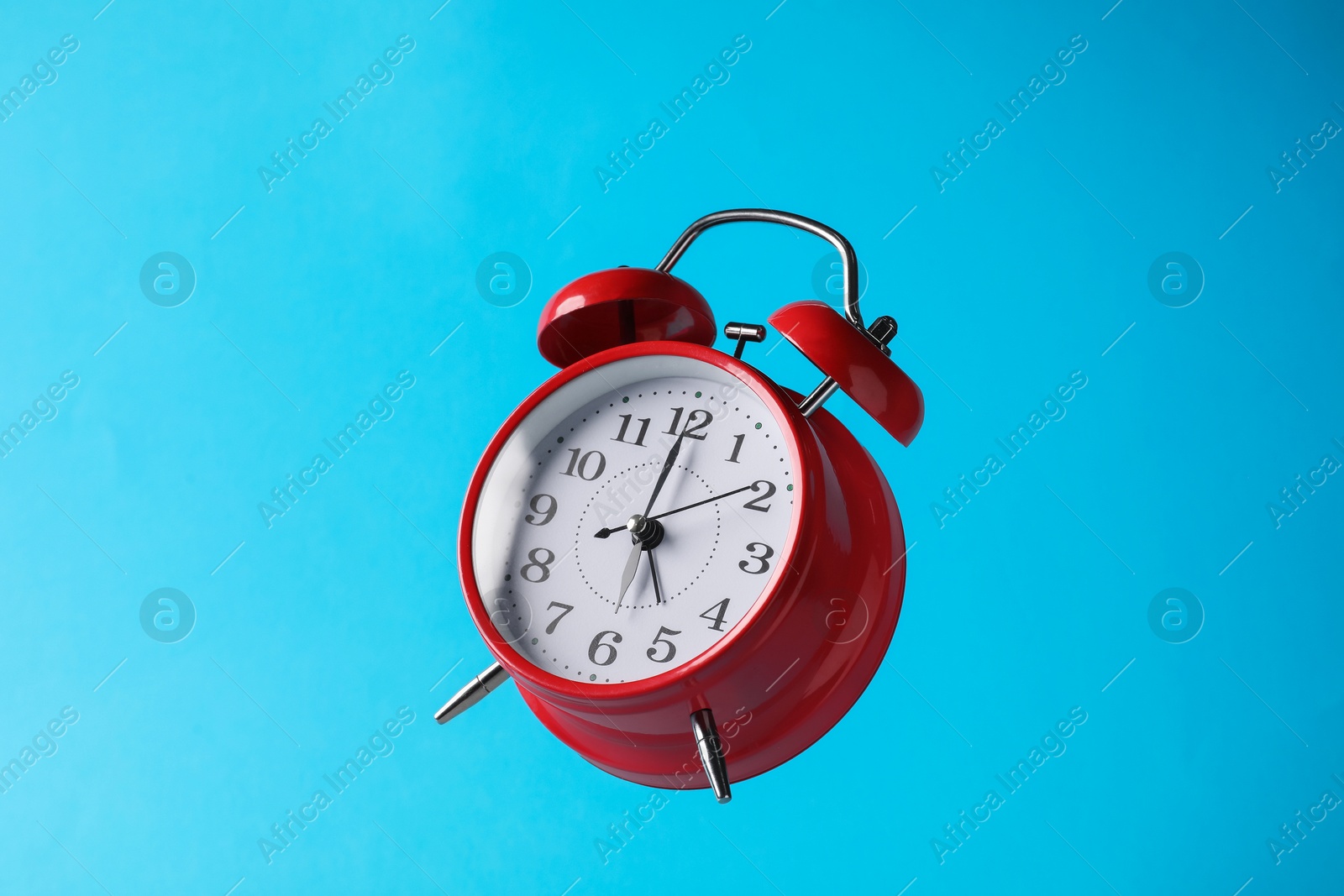 Photo of Red alarm clock in air on light blue background