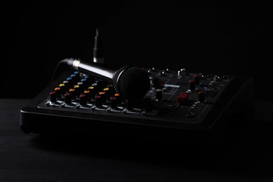 Photo of Professional mixing console with microphone on table against black background, closeup