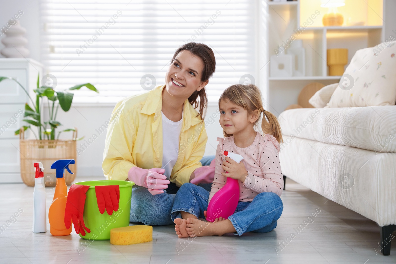 Photo of Little helper. Mother and her cute daughter with spray bottle of cleaning product on floor at home