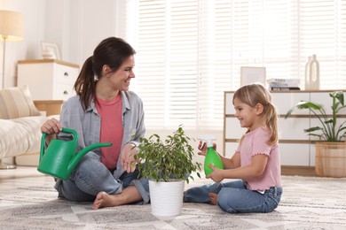 Photo of Cute little girl helping her mother watering houseplant at home