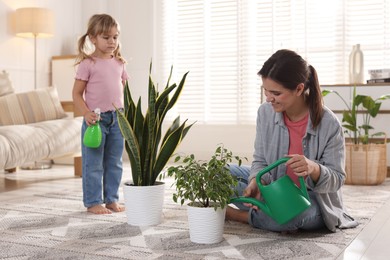 Photo of Cute little girl helping her mother watering houseplants at home, selective focus