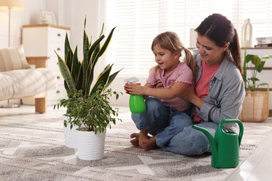 Cute little girl helping her mother watering houseplant at home