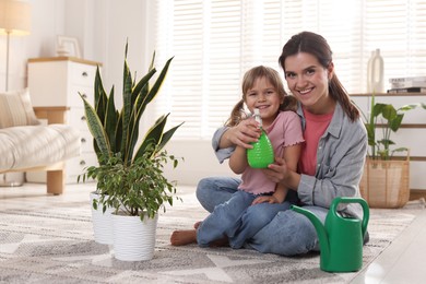 Photo of Little helper. Mother and her cute daughter with spray bottle near houseplants at home