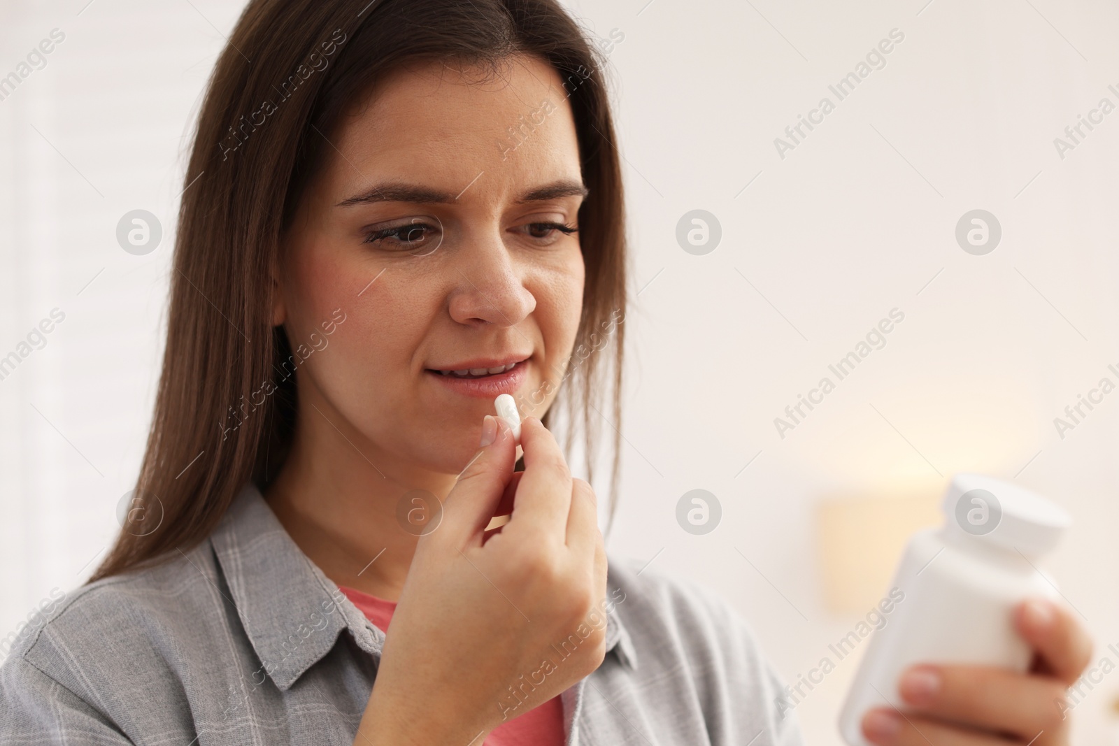 Photo of Woman reading medical instruction on plastic bottle while taking pill at home