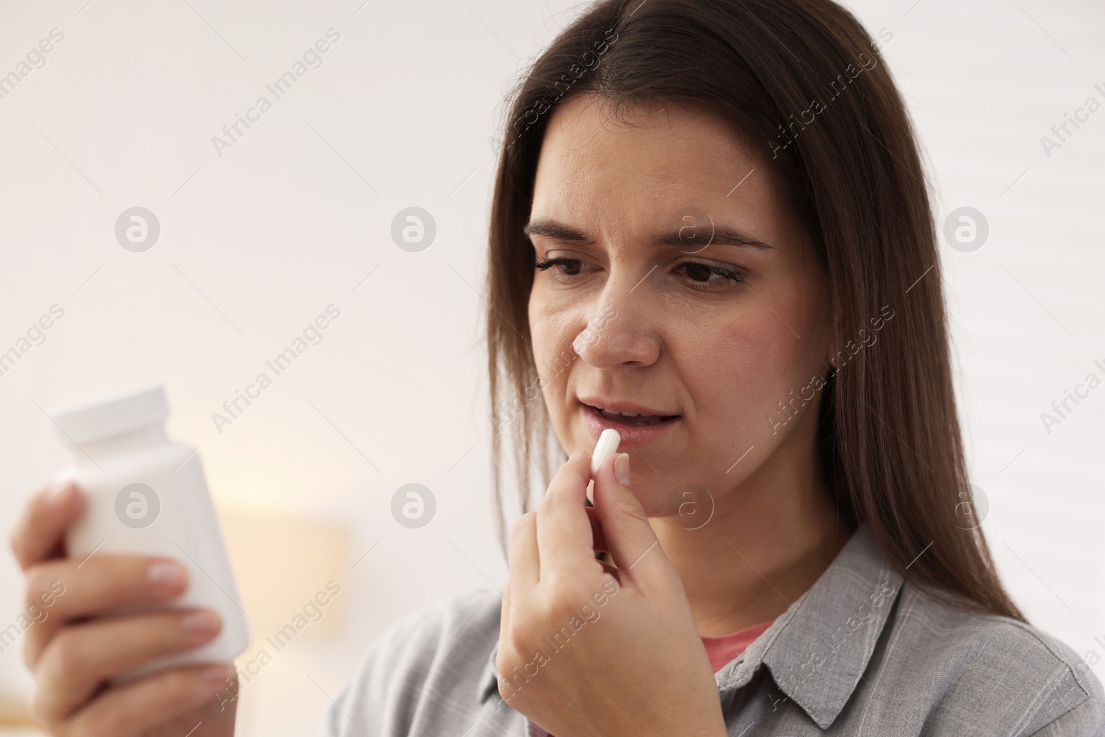 Photo of Woman reading medical instruction on plastic bottle while taking pill at home