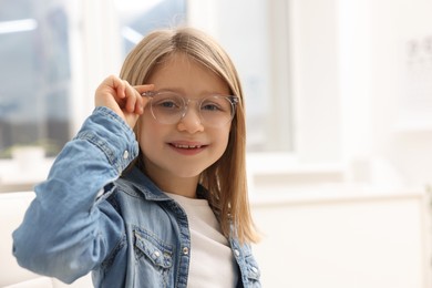 Photo of Little girl trying glasses at ophthalmologist office, space for text