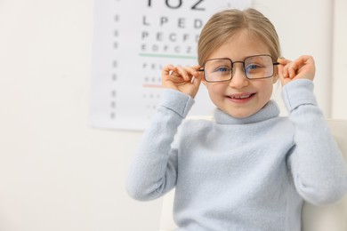 Photo of Little girl trying glasses at ophthalmologist office, space for text